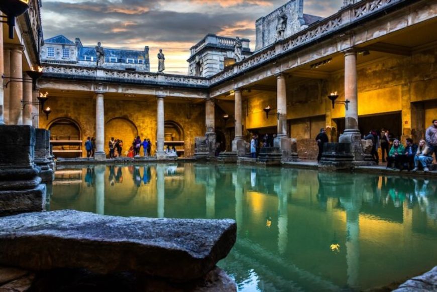 people standing around the roman baths at sunset